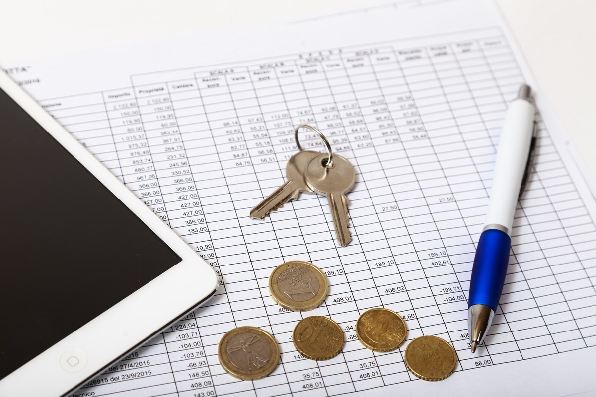 Prospetto di ripartizione spese per scale con chiavi, monete in euro, penna blu e tablet bianco su una scrivania